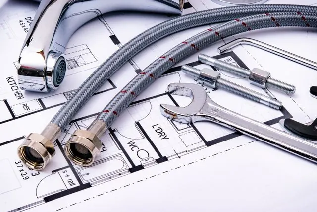 Faucet, braided supply hoses and wrenches laid on a bathroom floor plan