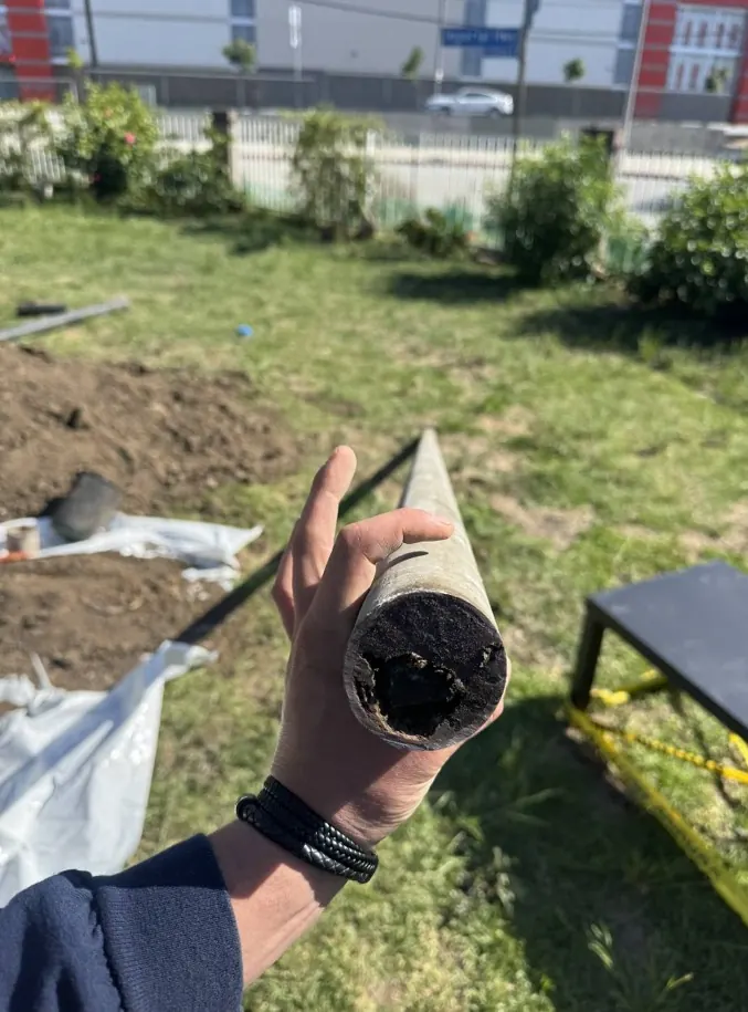Hand holding a cut section of drain pipe packed with buildup