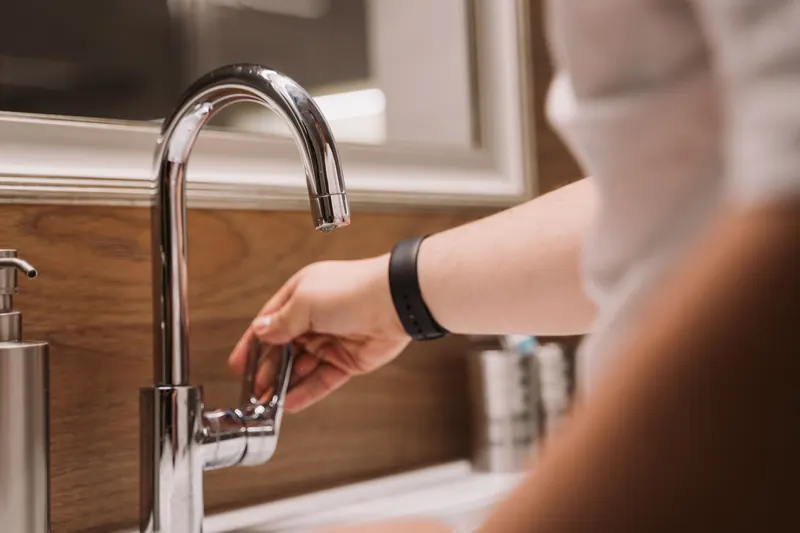 Hand turning on a chrome kitchen faucet