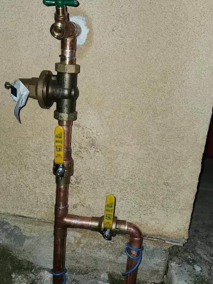 Copper main water line with a brass shutoff valve and pressure regulator at the house wall