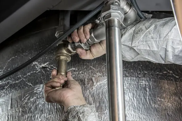 Hands tightening a brass fitting on a supply pipe under a house