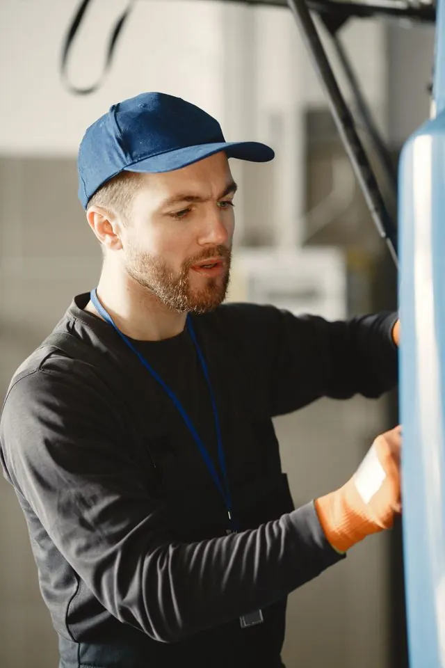 Plumber in a cap and work gloves inspecting a tank water heater