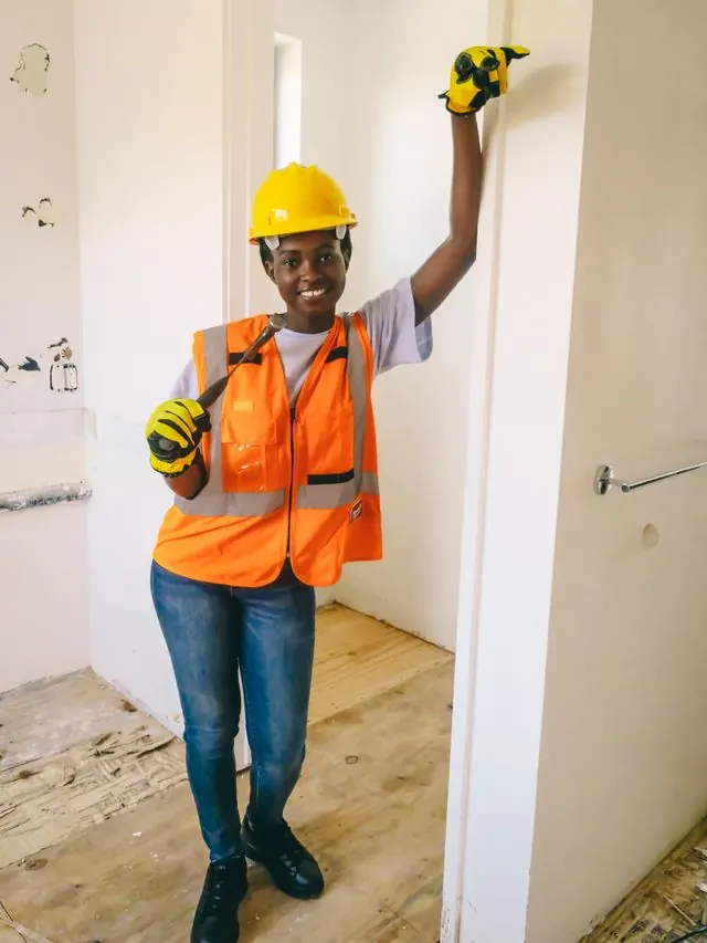 Plumber in a hard hat and safety vest holding up a wrench in a room under renovation