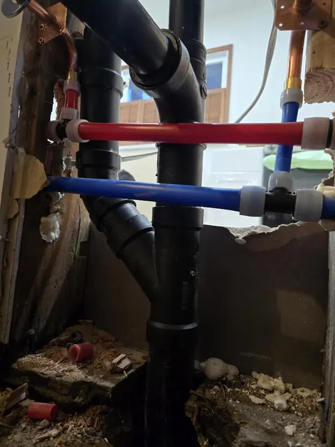 Red and blue PEX water lines beside black ABS drain pipes in an opened wall