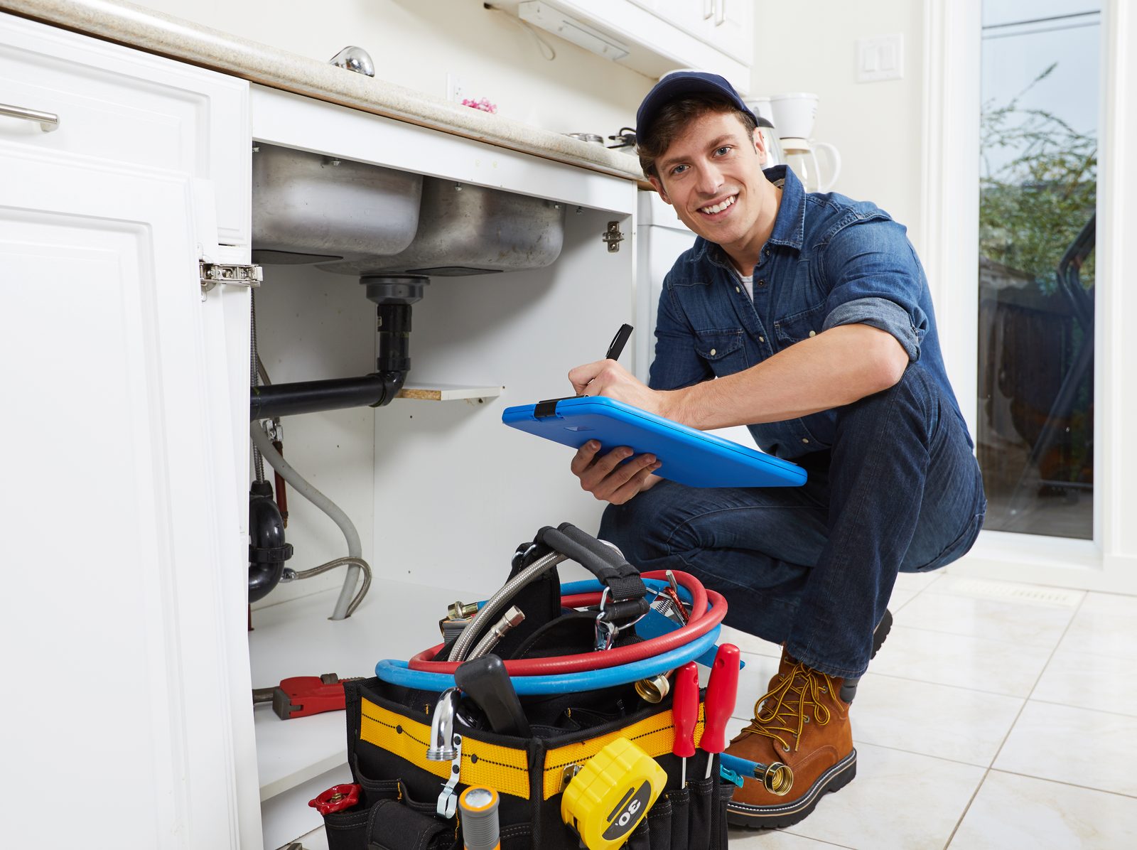 Smiling licensed plumber writing up an estimate under a kitchen sink