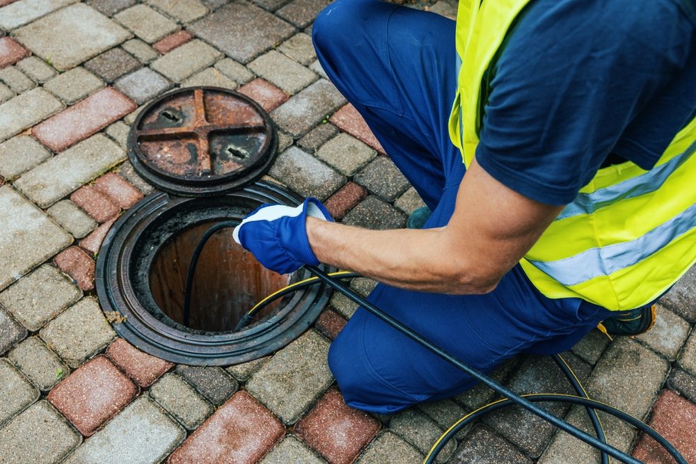 Plumber feeding a drain cable into a sewer cleanout to clear a mainline blockage