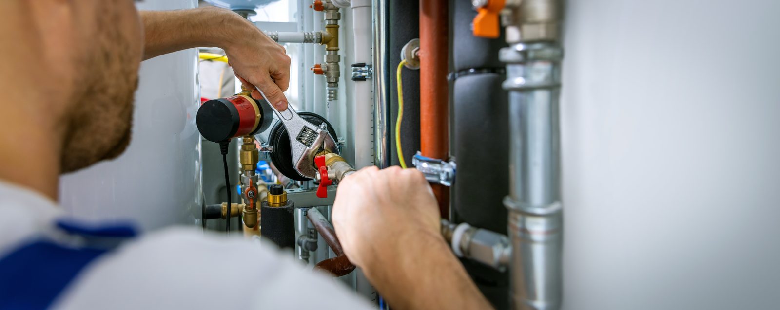 Plumber using a wrench to service a circulating pump and valves on a water heater system