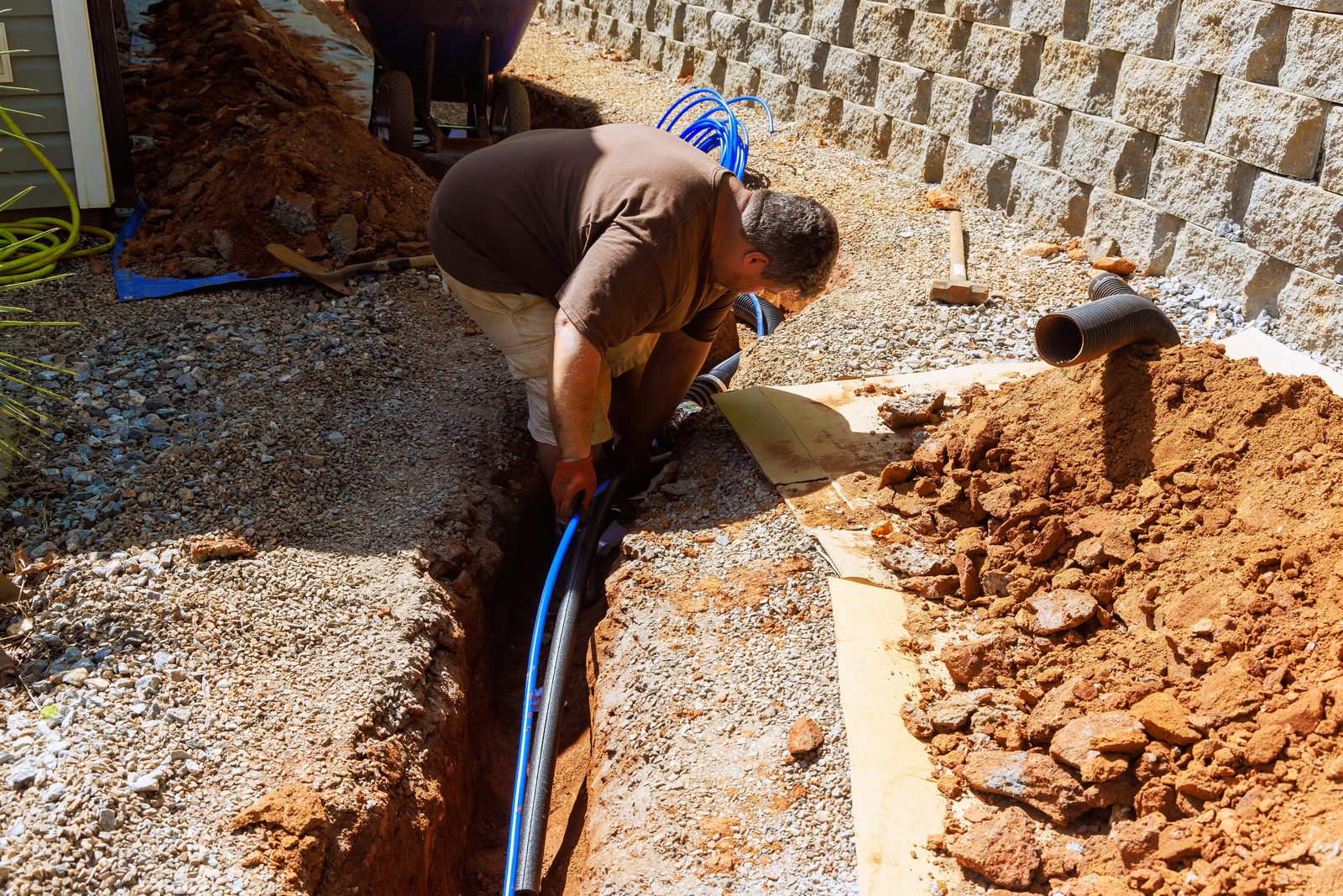 Plumber laying a new blue water service line in a trench alongside a home